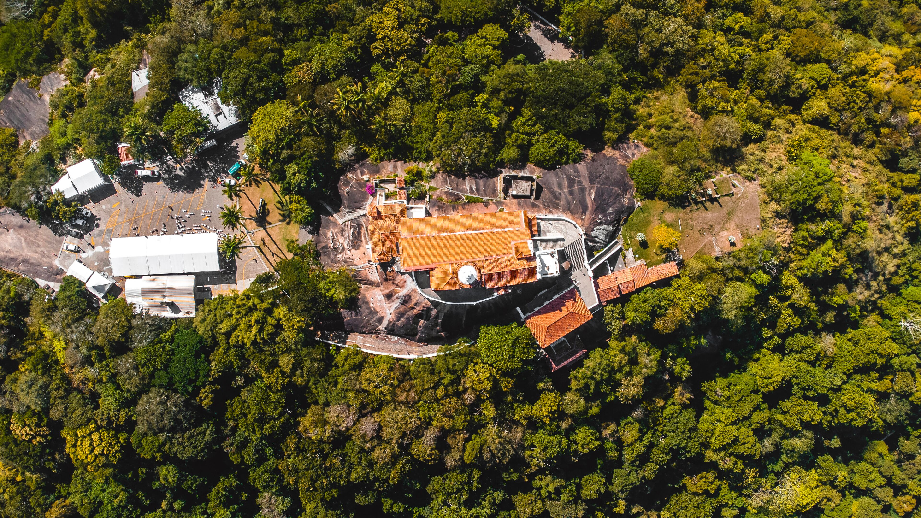 An aerial view of a forested area with a large building featuring a red roof and a circular structure.