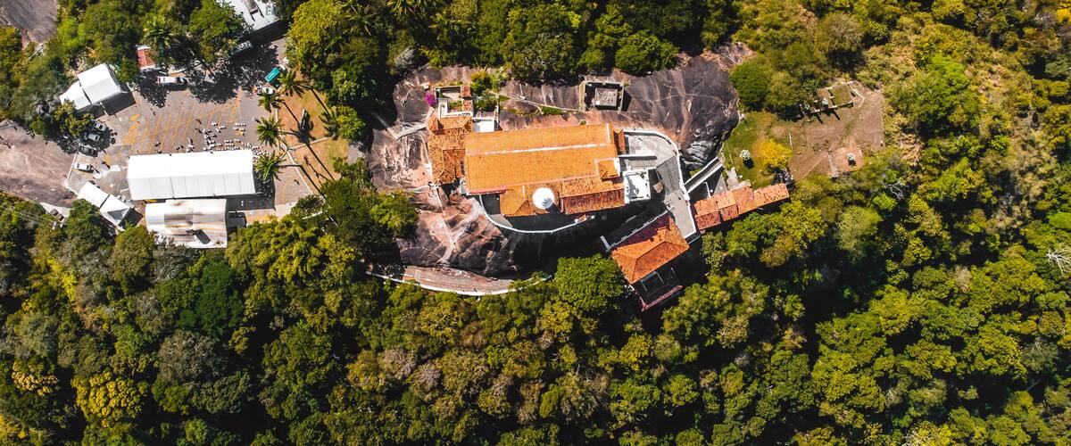 An aerial view of a forested area with a large building featuring a red roof and a circular structure.