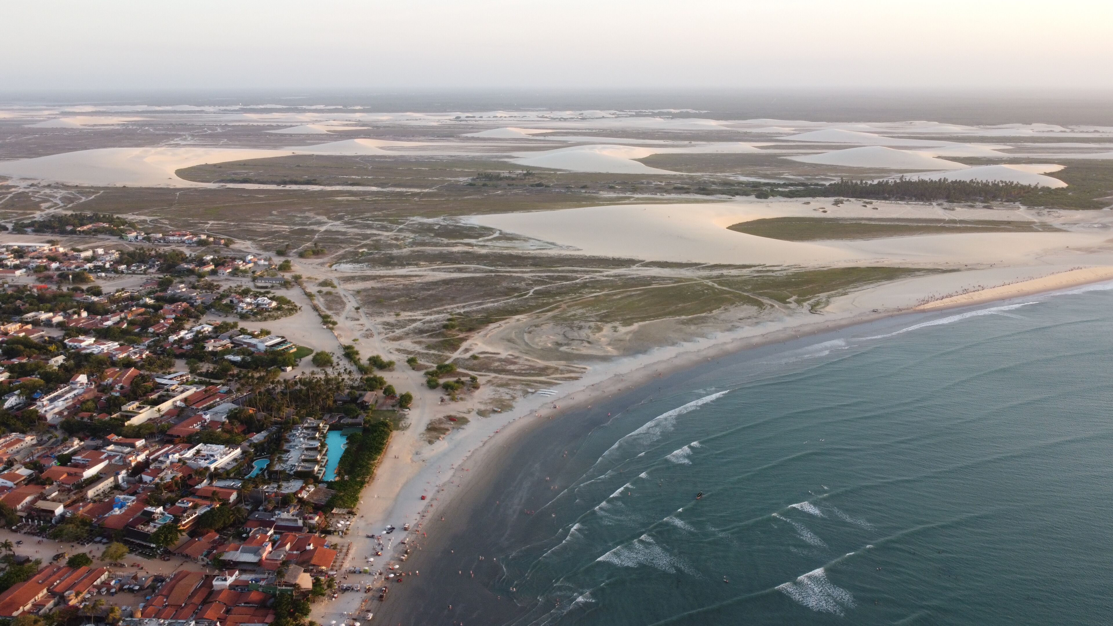 An aerial view of a coastal town with a beach, dunes, and a large body of water.