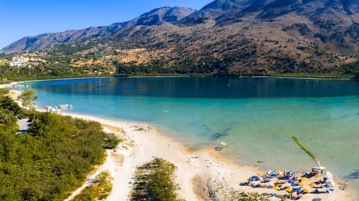 Ein See, umgeben von Bergen, ein Strand mit Sonnenschirmen und Booten.