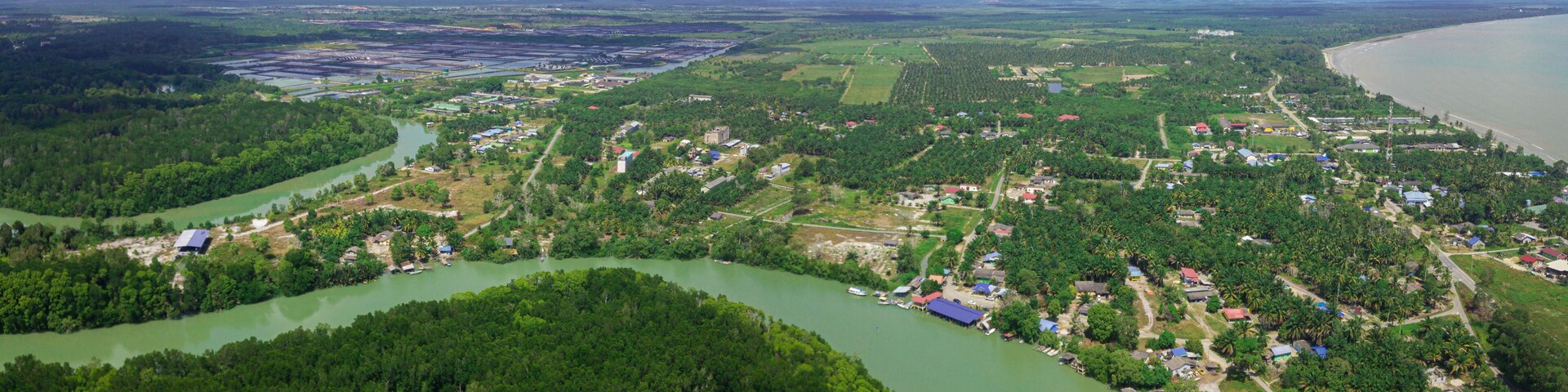 Vista aérea de uma vila costeira com um rio, campos verdes e edifícios dispersos.