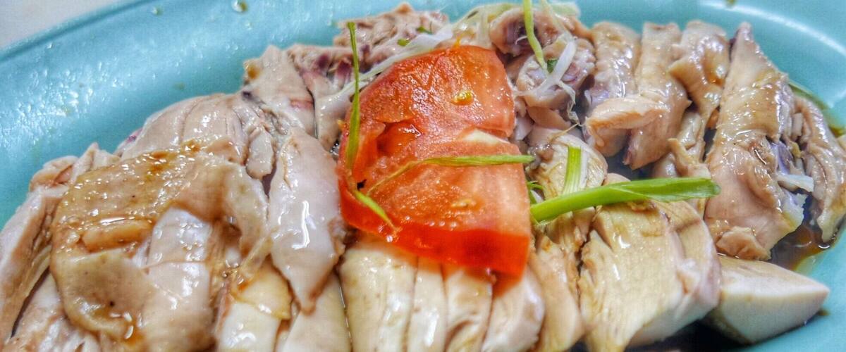 A plate of sliced chicken with a garnish of tomato and green onions.