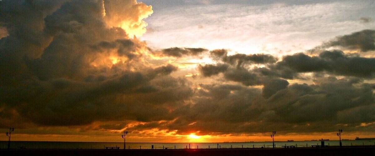A sunset over a beach with a large cloud formation.