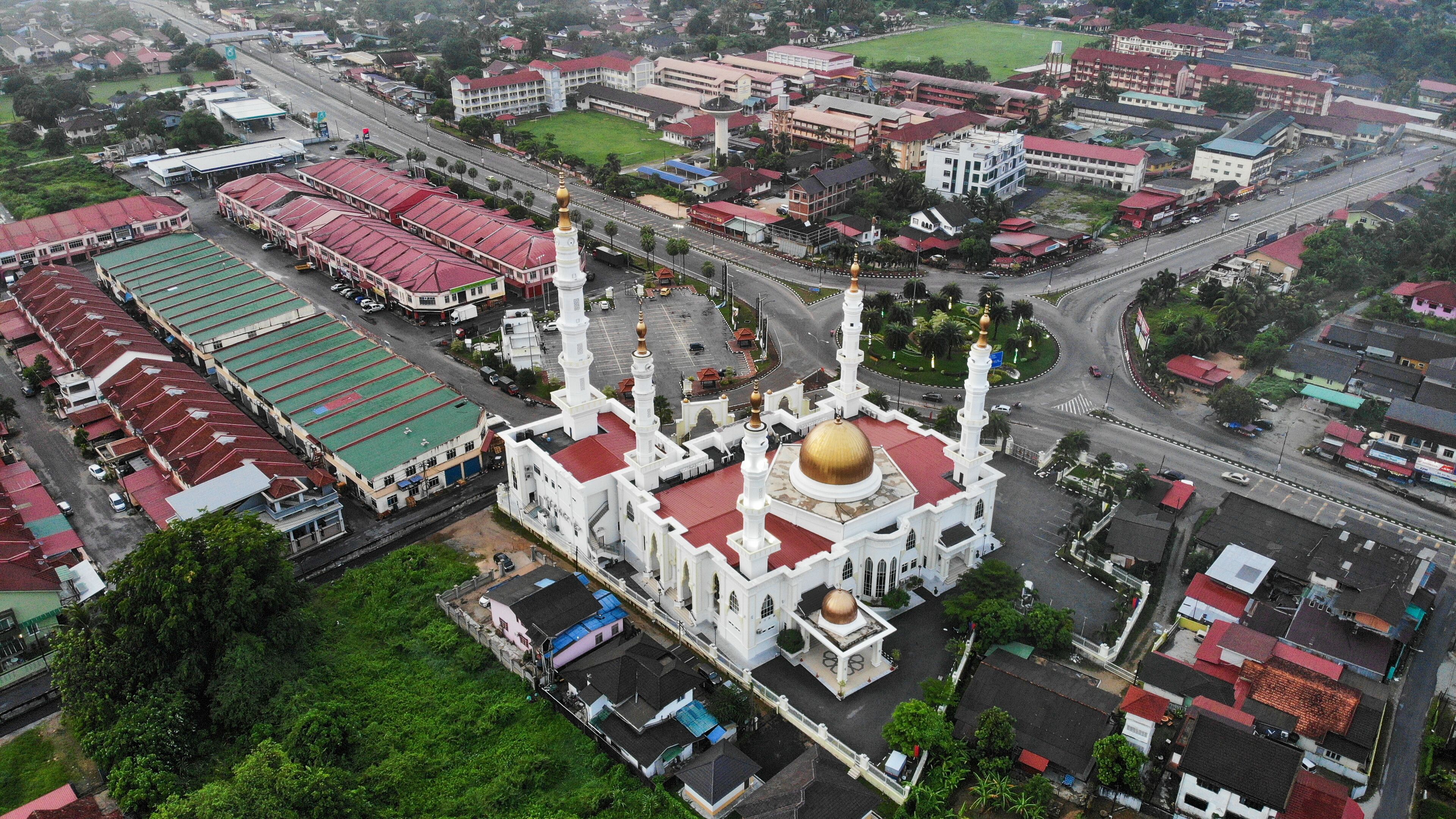An aerial view of a city with a prominent white mosque with a golden dome and minarets, surrounded by residential and commercial buildings.