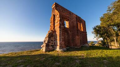 A brick ruin by a lake with a clear sky.
