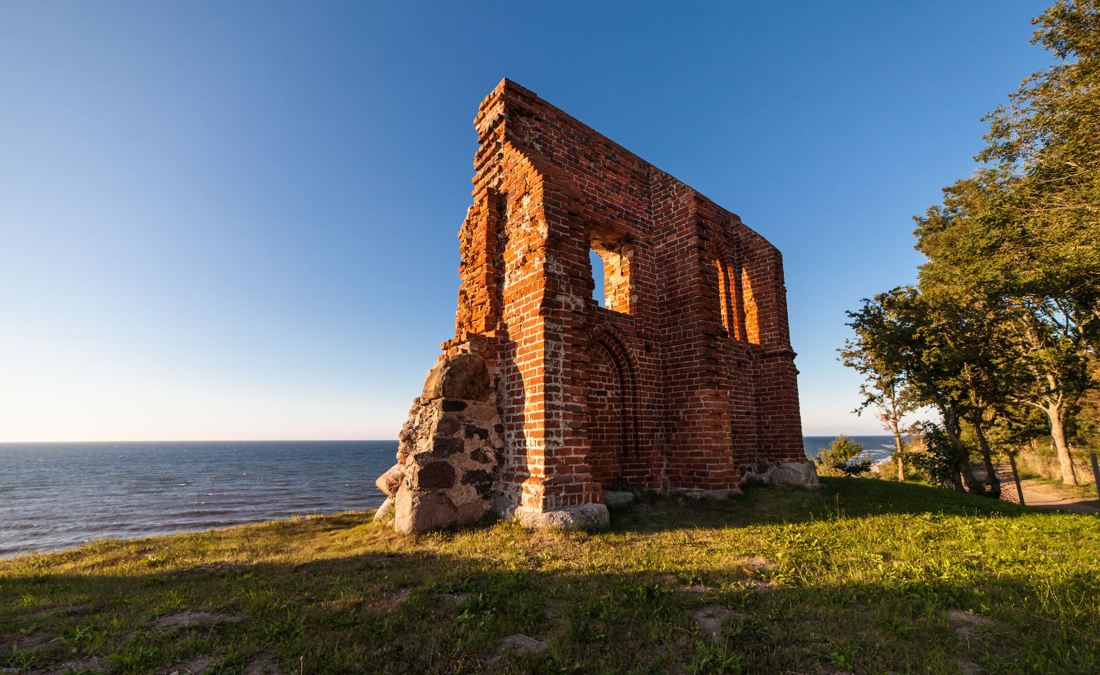 A brick ruin by a lake with a clear sky.