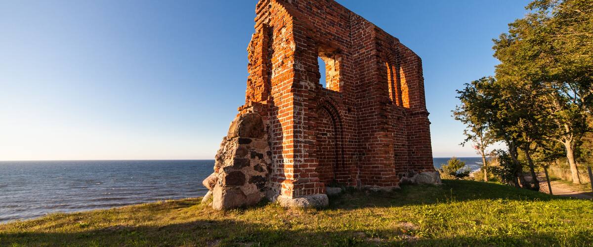 A brick ruin by a lake with a clear sky.