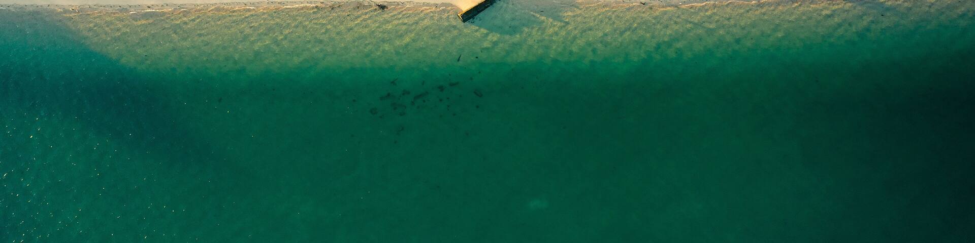 An aerial view of a beach with a lifeguard tower, a boat, and beach umbrellas.