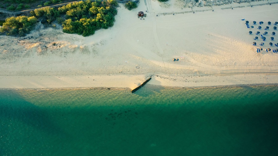 Vista aérea de uma praia com uma torre de salva-vidas, um barco e guarda-sóis.
