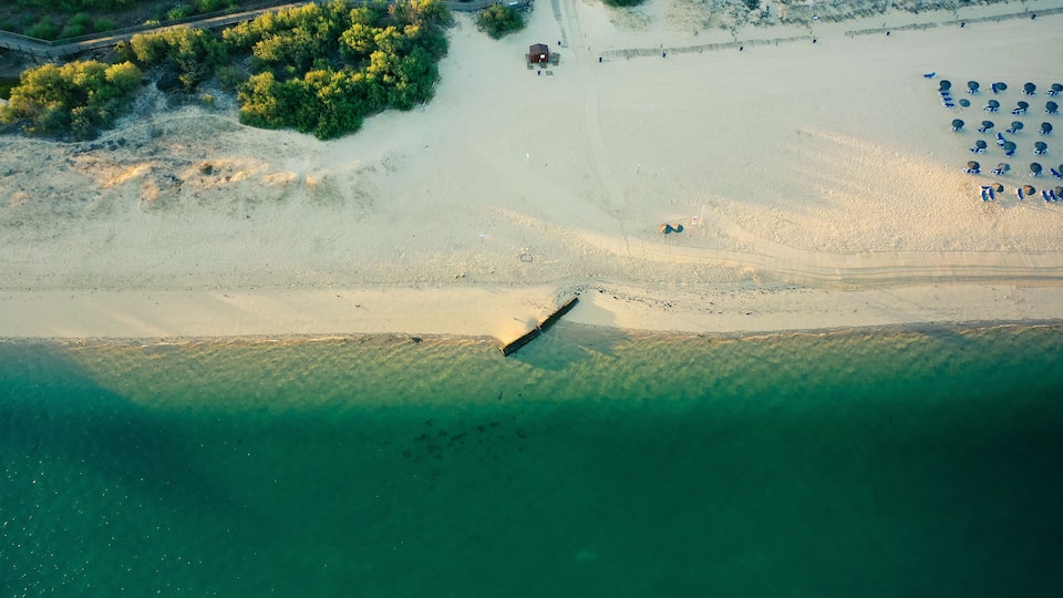 An aerial view of a beach with a lifeguard tower, a boat, and beach umbrellas.