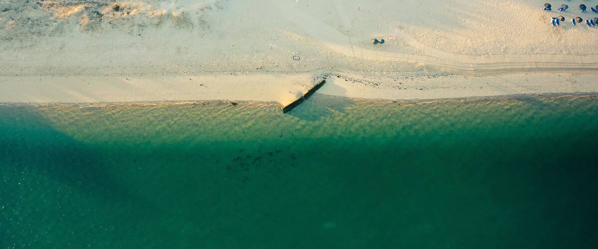 An aerial view of a beach with a lifeguard tower, a boat, and beach umbrellas.