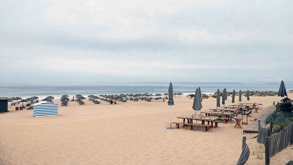 A beach with umbrellas, tables, and a striped building.