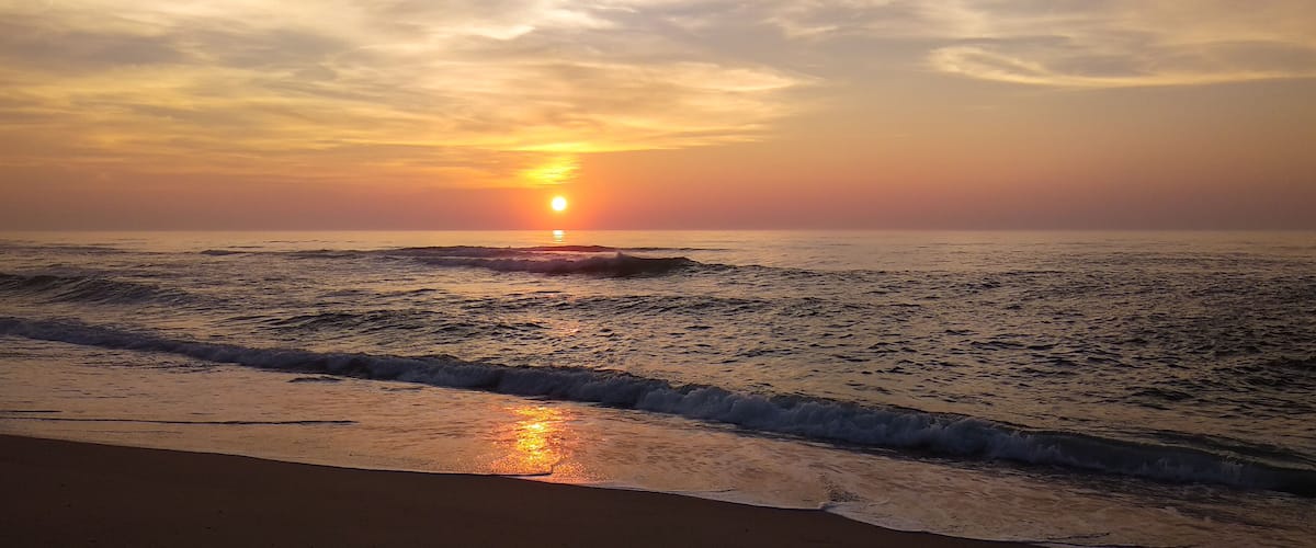 A beach at sunset with waves and a clear sky.
