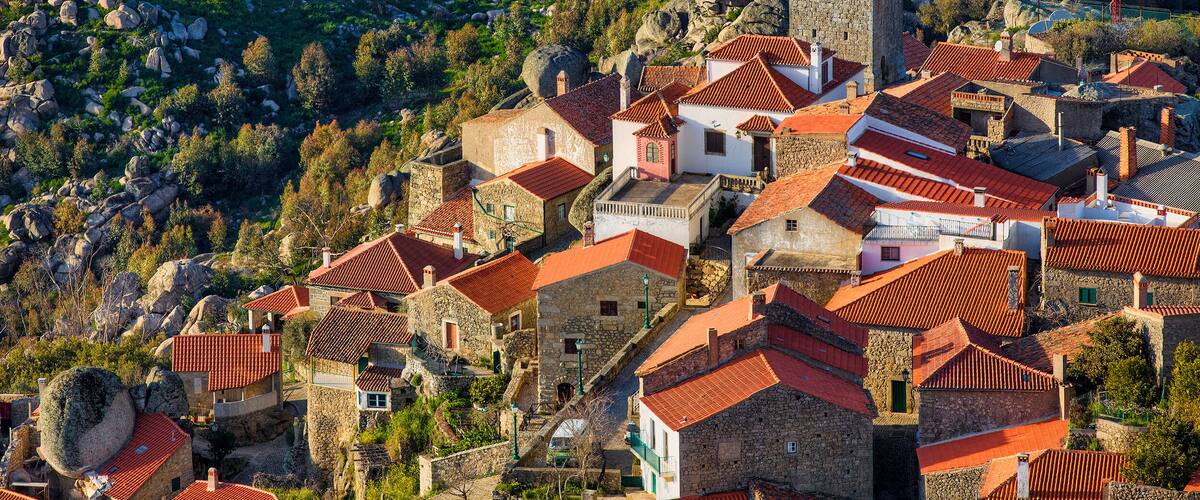 A mountainous village with stone buildings and red-tiled roofs, surrounded by rocky terrain and greenery.
