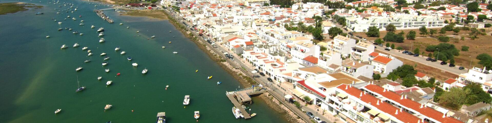 A coastal town with a marina filled with boats, white buildings with red roofs, and a clear blue sky.
