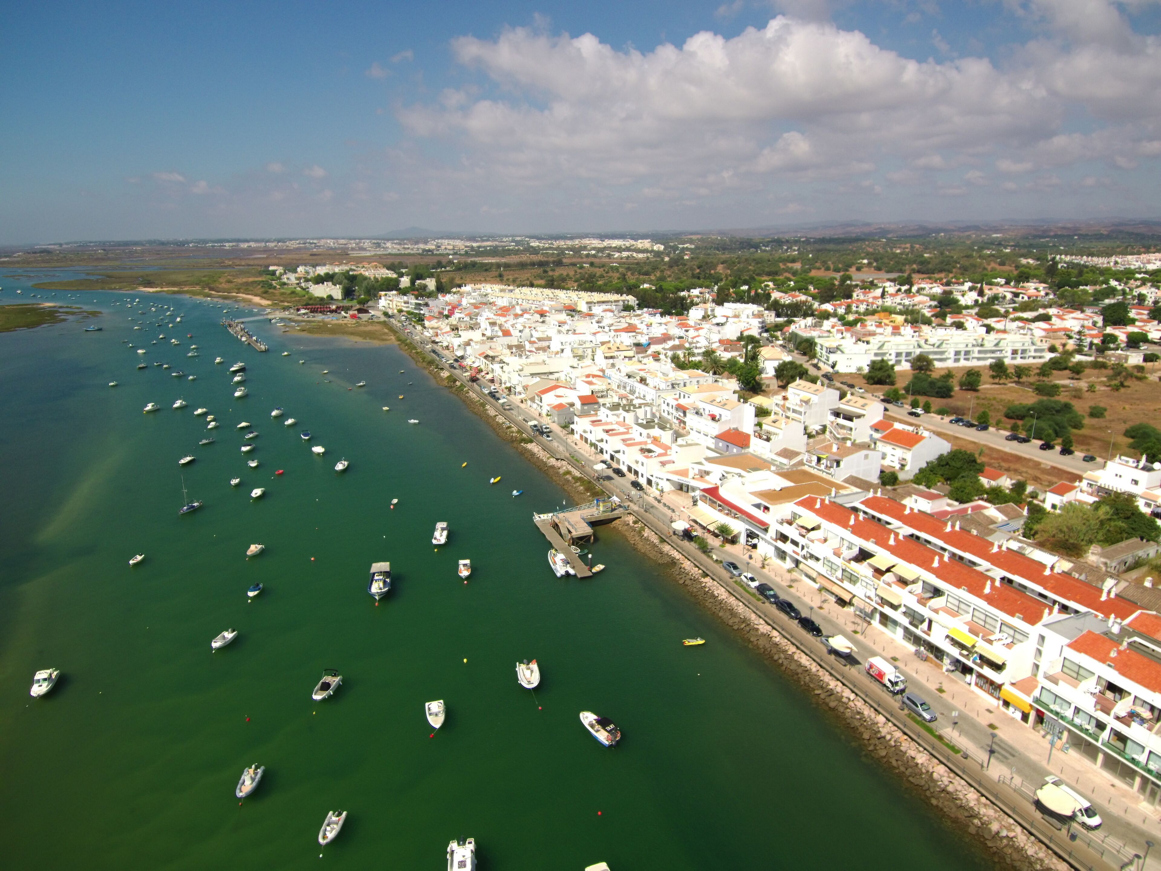 A coastal town with a marina filled with boats, white buildings with red roofs, and a clear blue sky.