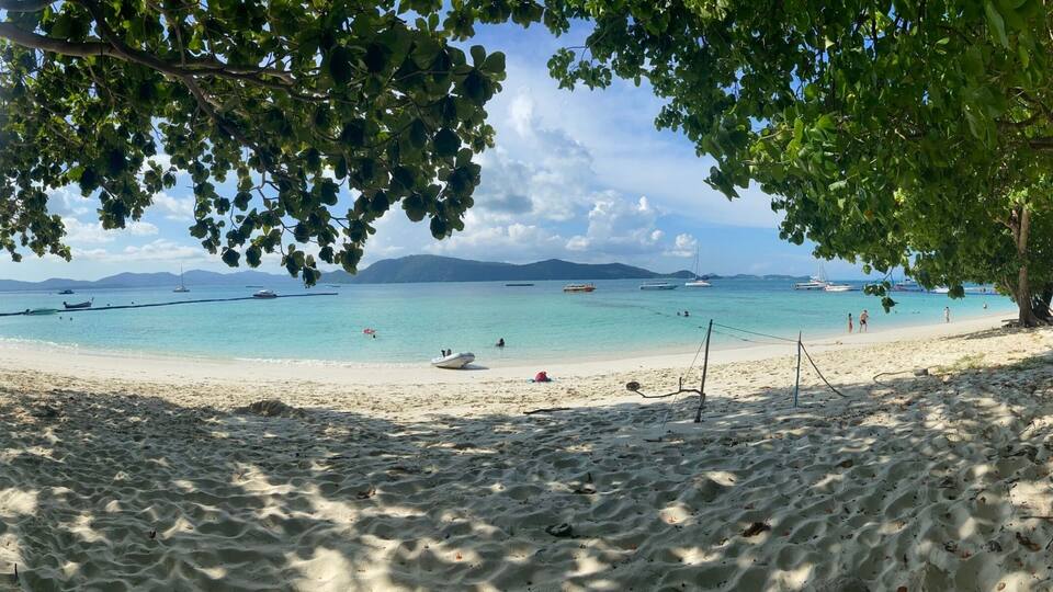 A beach with clear turquoise water, boats, and people.