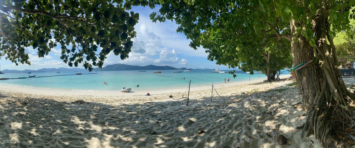 A beach with clear turquoise water, boats, and people.