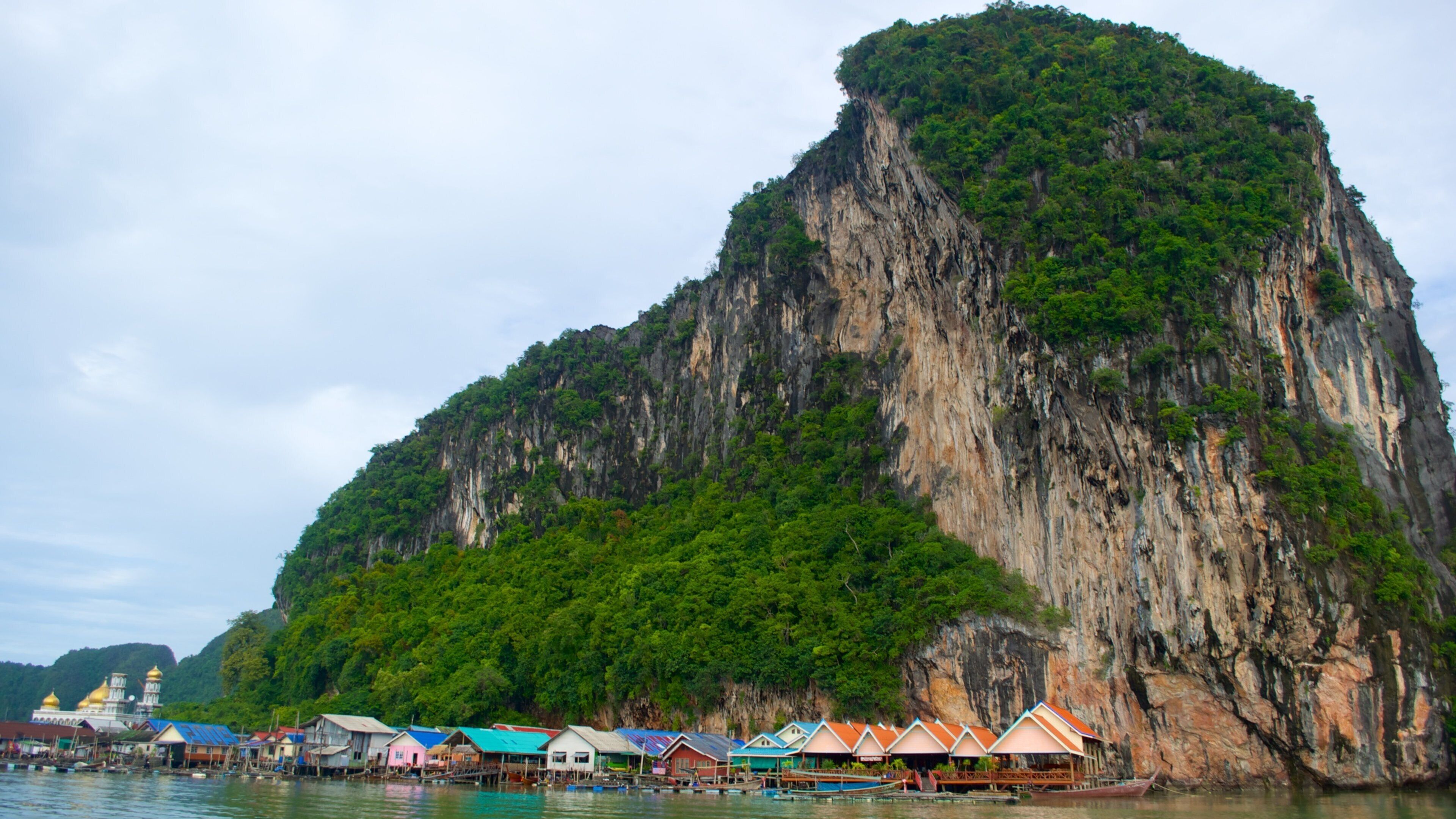 A coastal village with colorful houses and boats, surrounded by a large limestone cliff.
