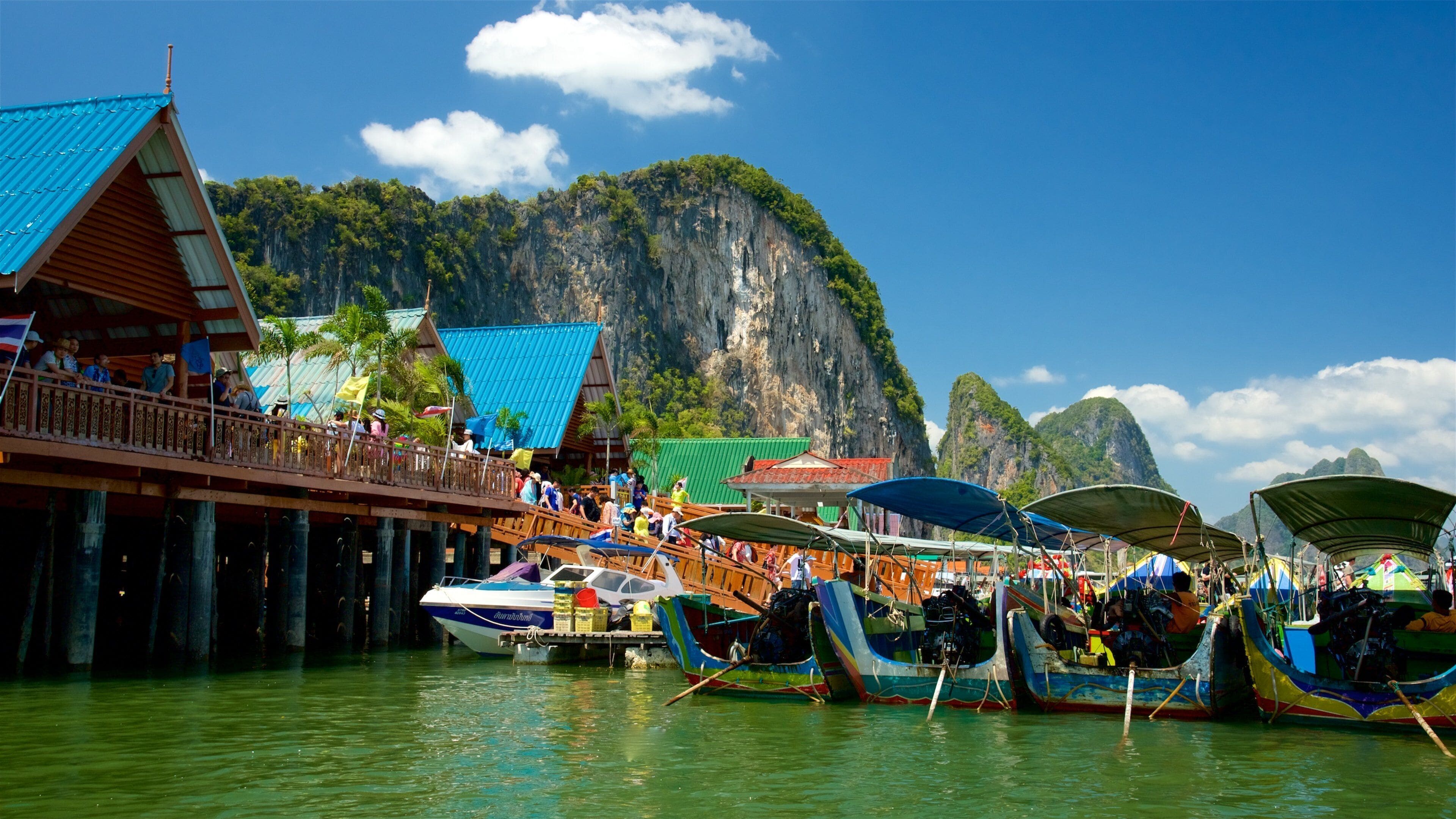 A floating market with boats docked in front of a mountain backdrop.