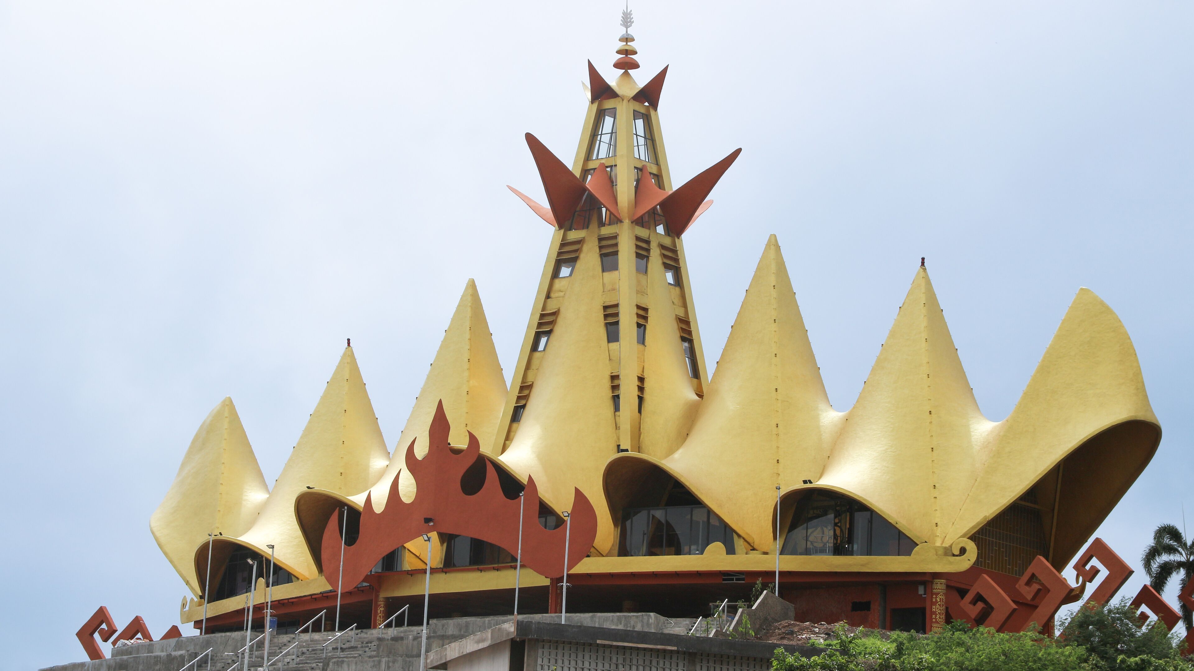 A yellow building with a unique, pointed roof design and a central tower.