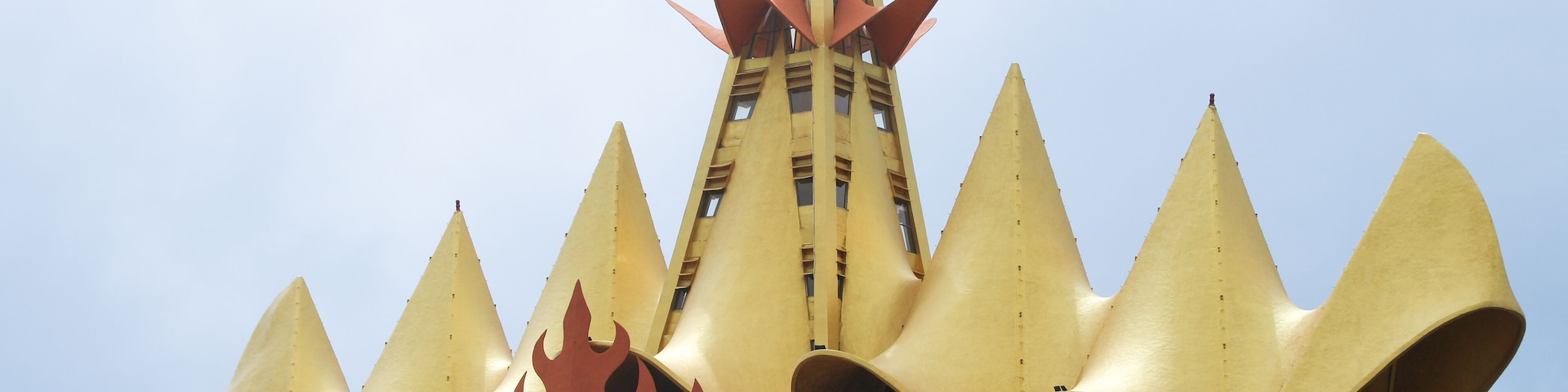A yellow building with a unique, pointed roof design and a central tower.