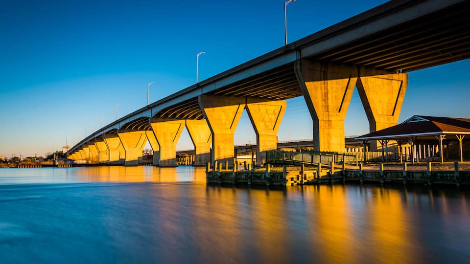 A long bridge with multiple arches over a calm body of water, illuminated by artificial lighting.