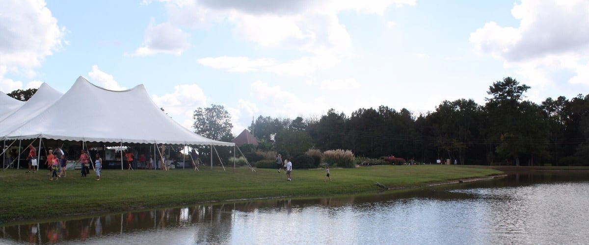 A lakeside area with tents and people walking near a pond.