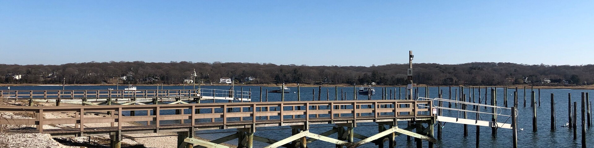 Un muelle de madera se extiende sobre un lago tranquilo bajo un cielo despejado.
