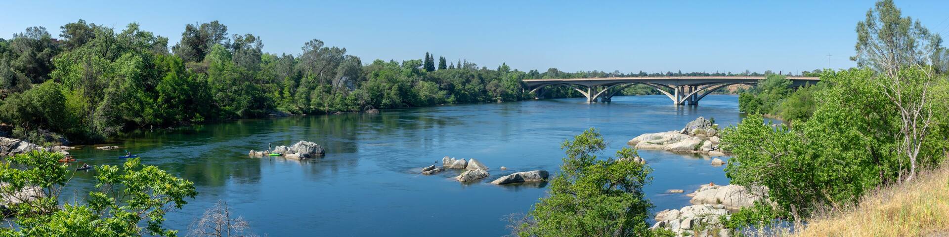 A river with a bridge, surrounded by dense green trees and rocks.