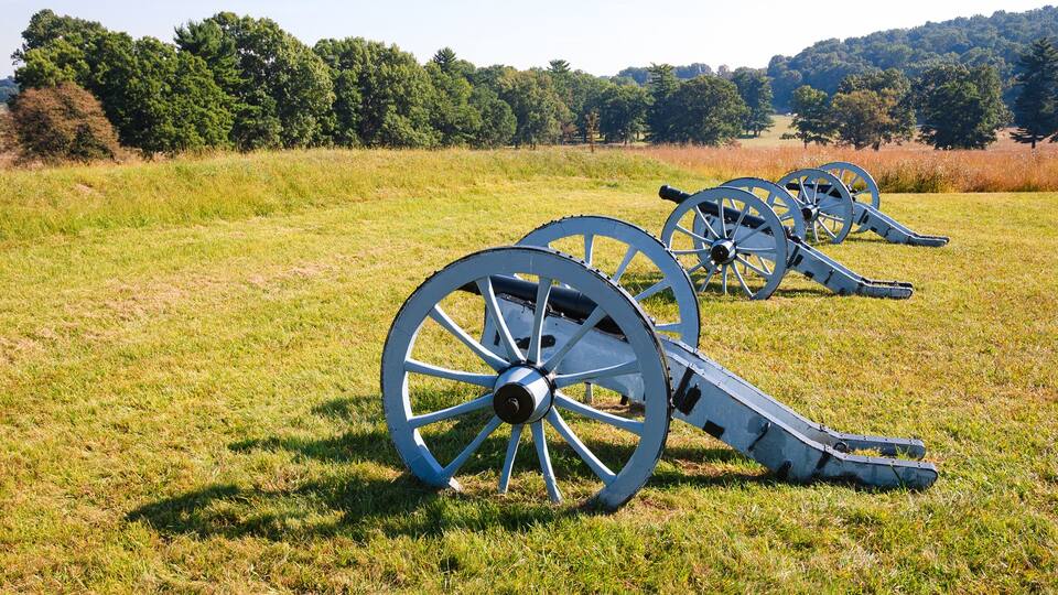 Three cannon wheels in a grassy field with trees in the background.