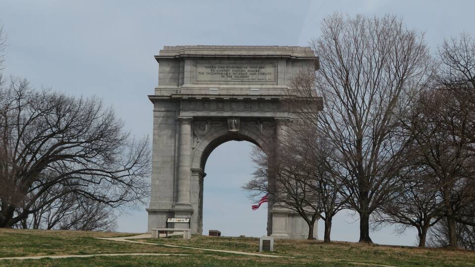 A large stone arch monument with an inscription, surrounded by trees and a grassy area.