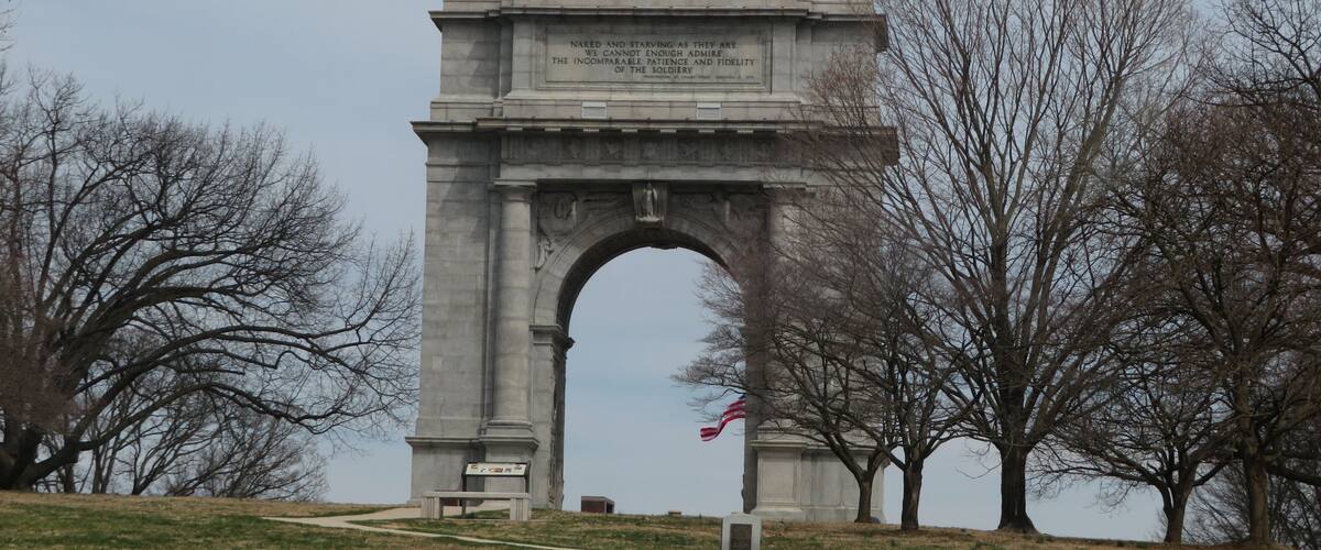 A large stone arch monument with an inscription, surrounded by trees and a grassy area.