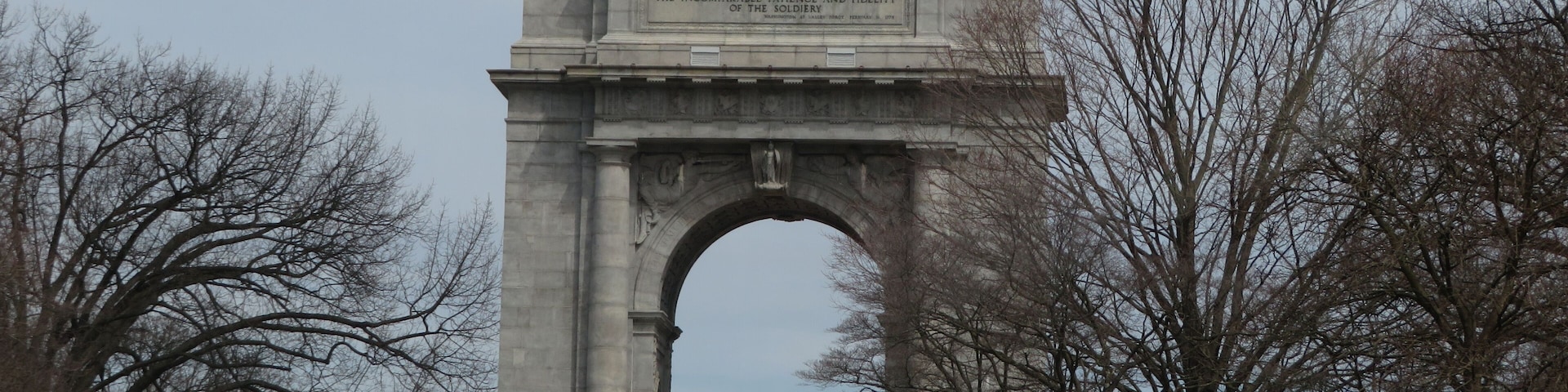 A large stone arch monument with an inscription, surrounded by trees and a grassy area.