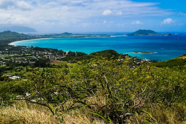 A coastal landscape with a clear view of turquoise waters, a sandy beach, and a town in the distance.