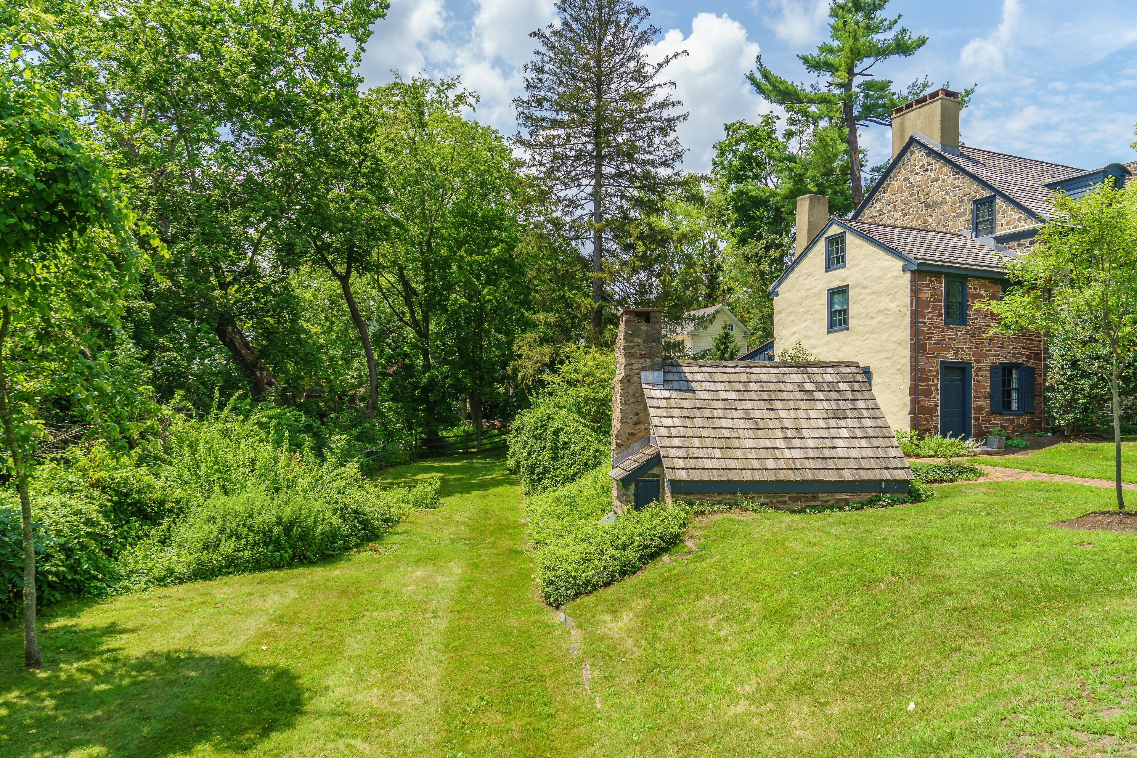 A house with a stone chimney, surrounded by lush greenery and tall trees.