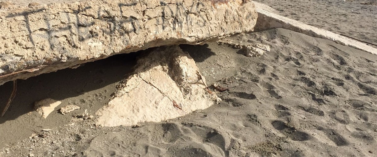 A large rock formation with carved inscriptions, located on a sandy beach with sparse vegetation.