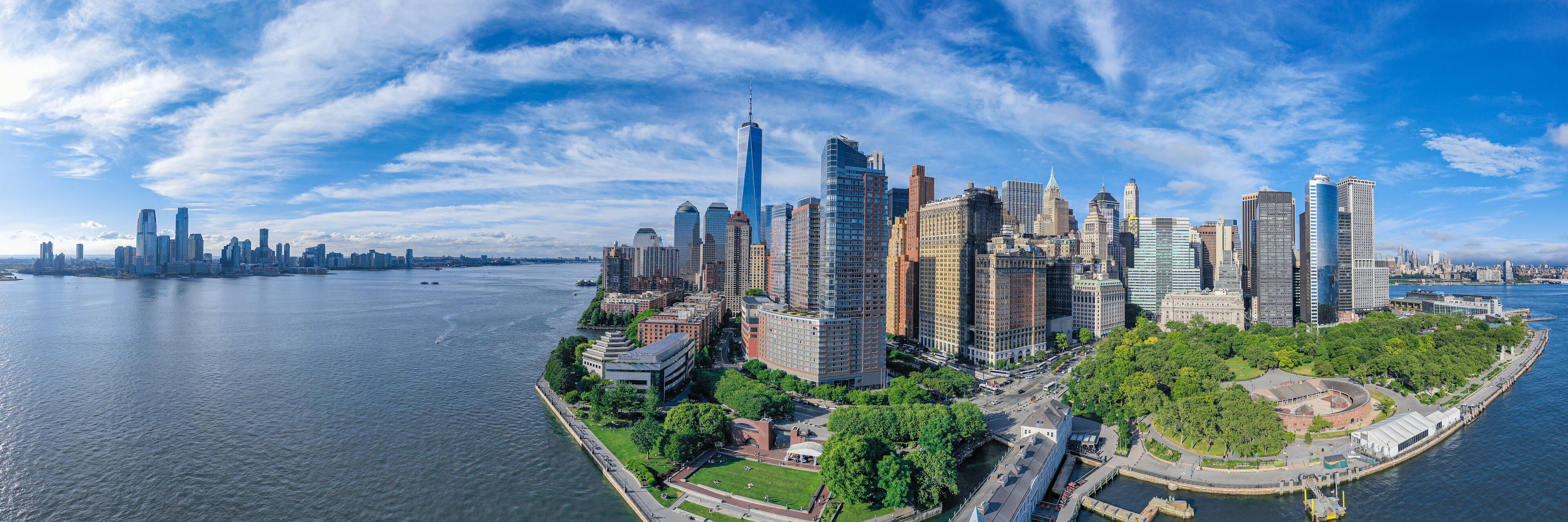 A panoramic view of a city skyline with a river, including prominent skyscrapers and a park area.