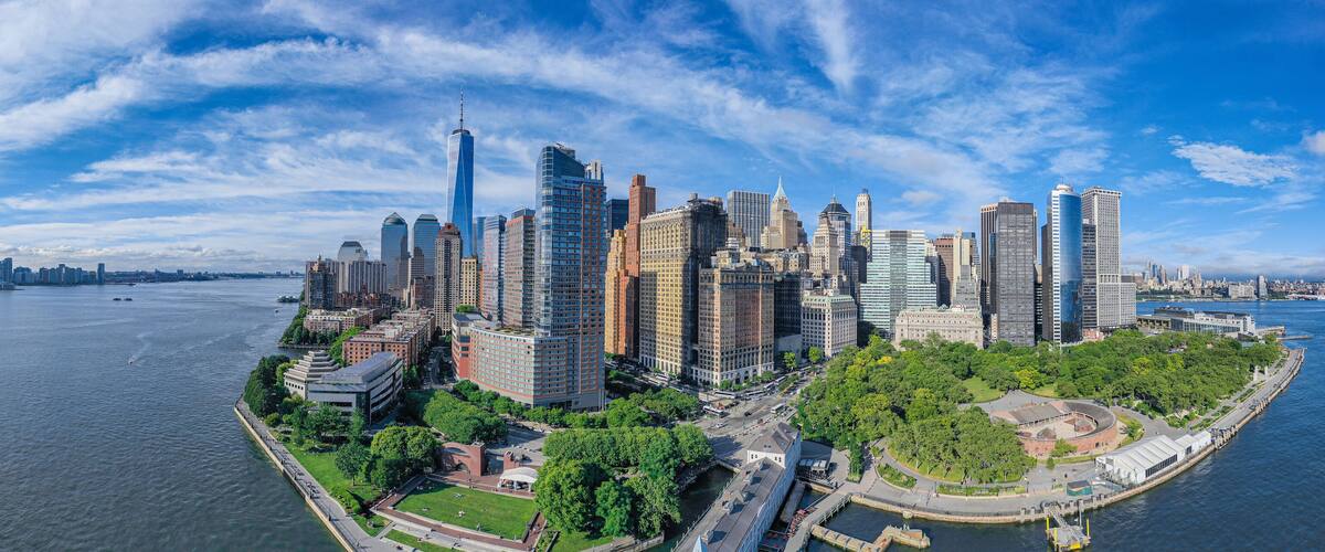 A panoramic view of a city skyline with a river, including prominent skyscrapers and a park area.