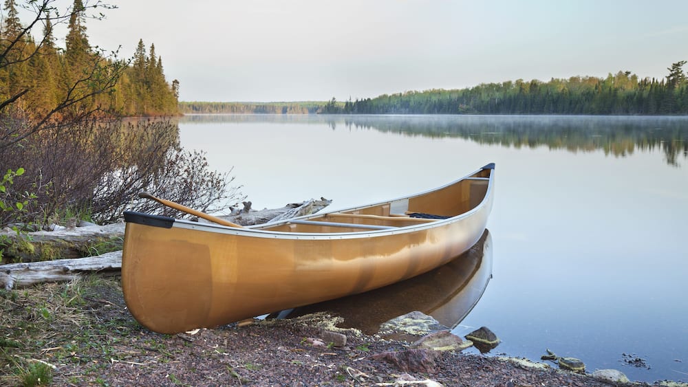 A canoe on a rocky shore by a calm lake with trees in the background.