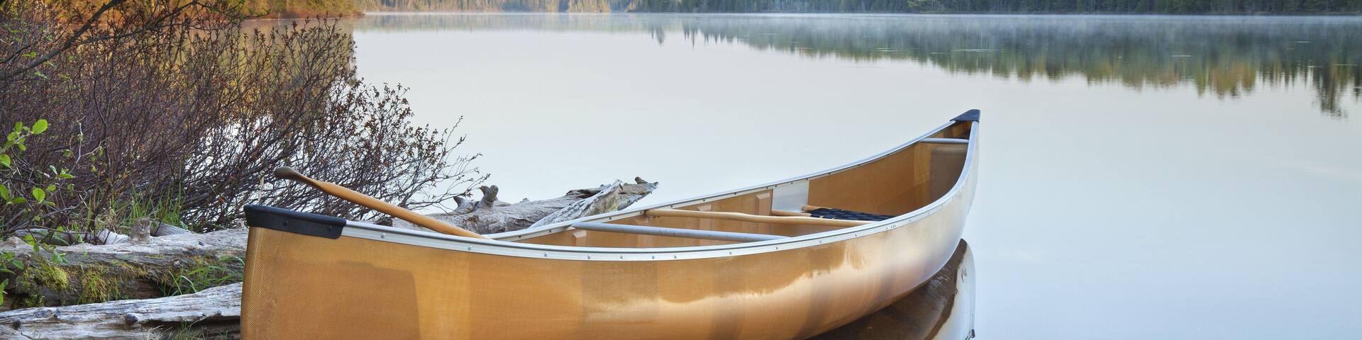 A canoe on a rocky shore by a calm lake with trees in the background.