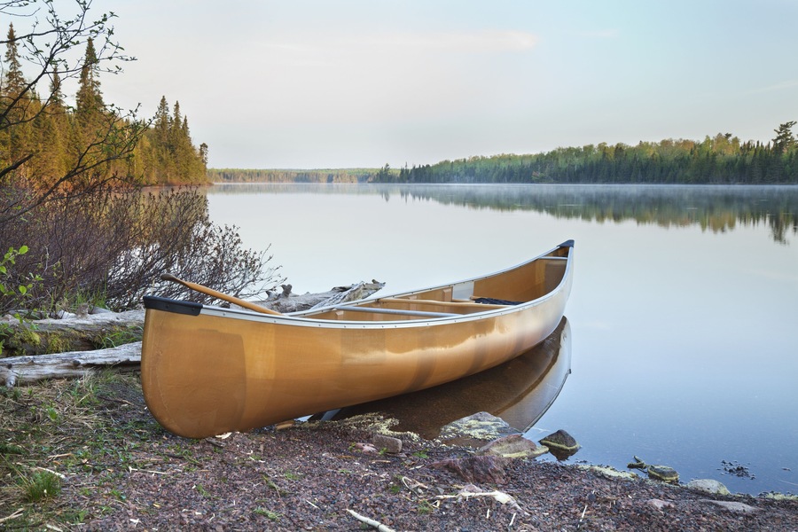 Kanootti kivikkoisella rannalla, tyynen järven äärellä, taustalla näkyy puita.