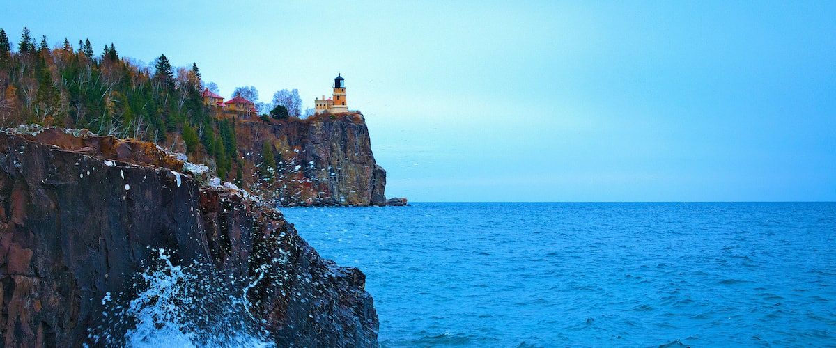 A rocky coastline with a lighthouse and ocean waves crashing against the shore.