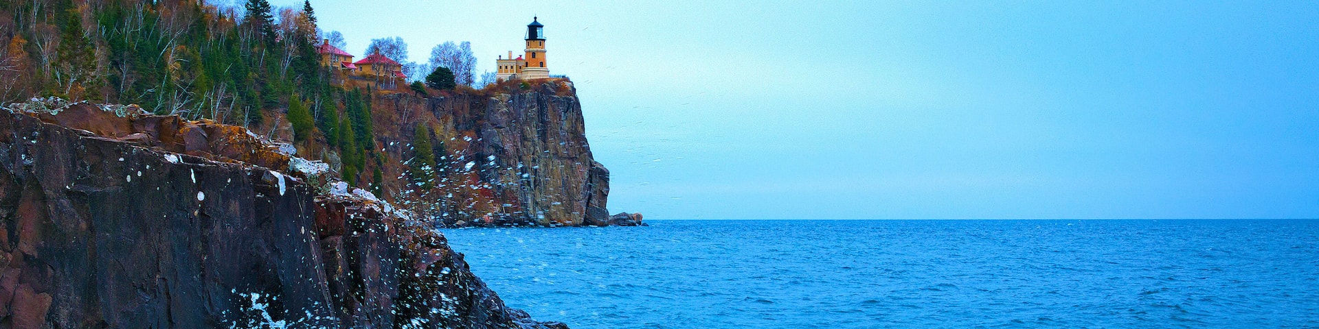 A rocky coastline with a lighthouse and ocean waves crashing against the shore.