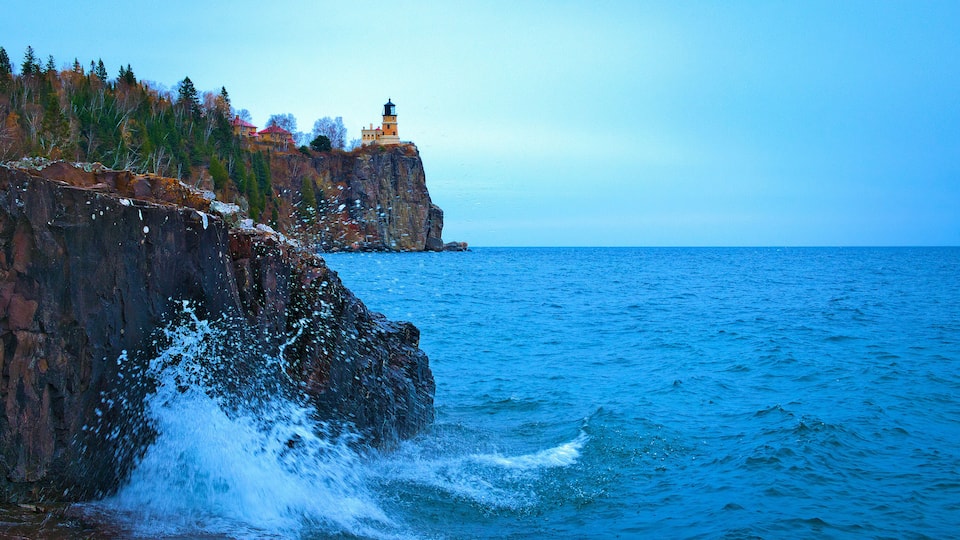 A rocky coastline with a lighthouse and ocean waves crashing against the shore.