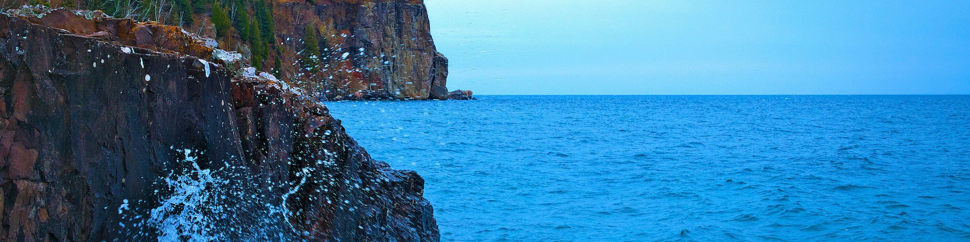Um litoral rochoso com um farol e ondas oceânicas quebrando na costa.