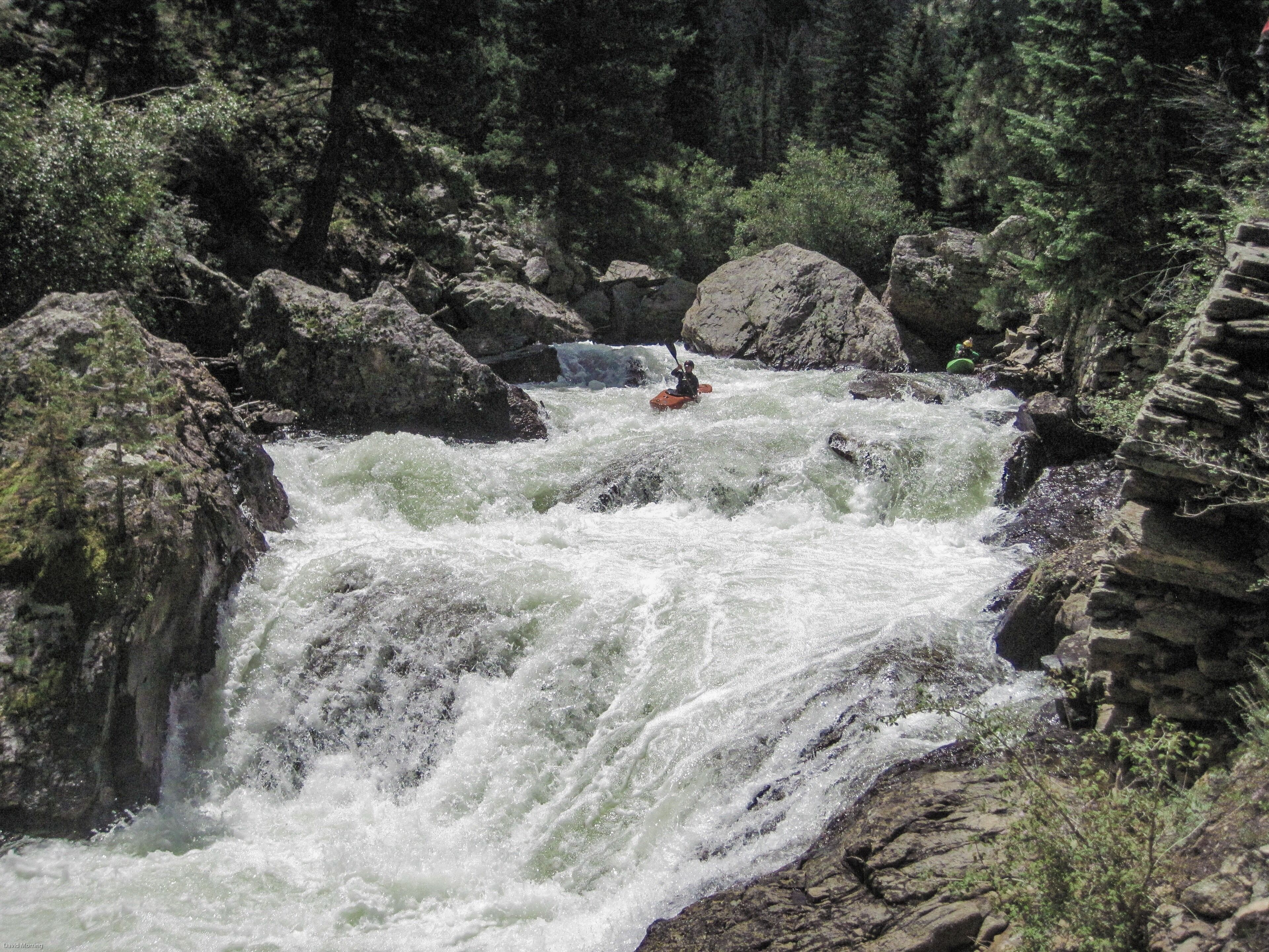 A white water rafting scene with a person in an orange raft navigating through a rocky river.