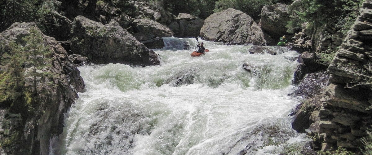 A white water rafting scene with a person in an orange raft navigating through a rocky river.