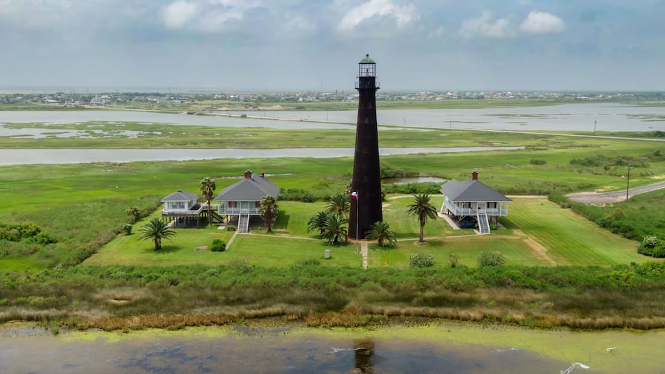 A lighthouse, two houses, and a marshy landscape.