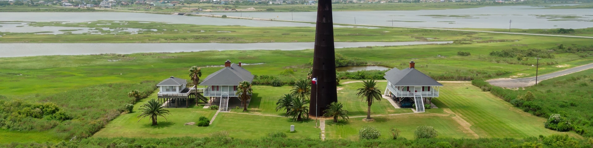 Ein Leuchtturm, zwei Häuser und eine sumpfige Landschaft.